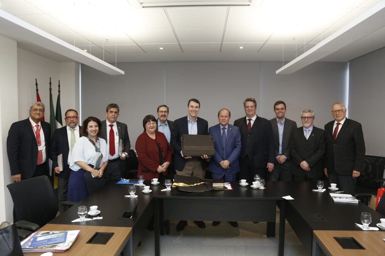 12 pessoas de pé atrás de mesas de reunião posando para foto