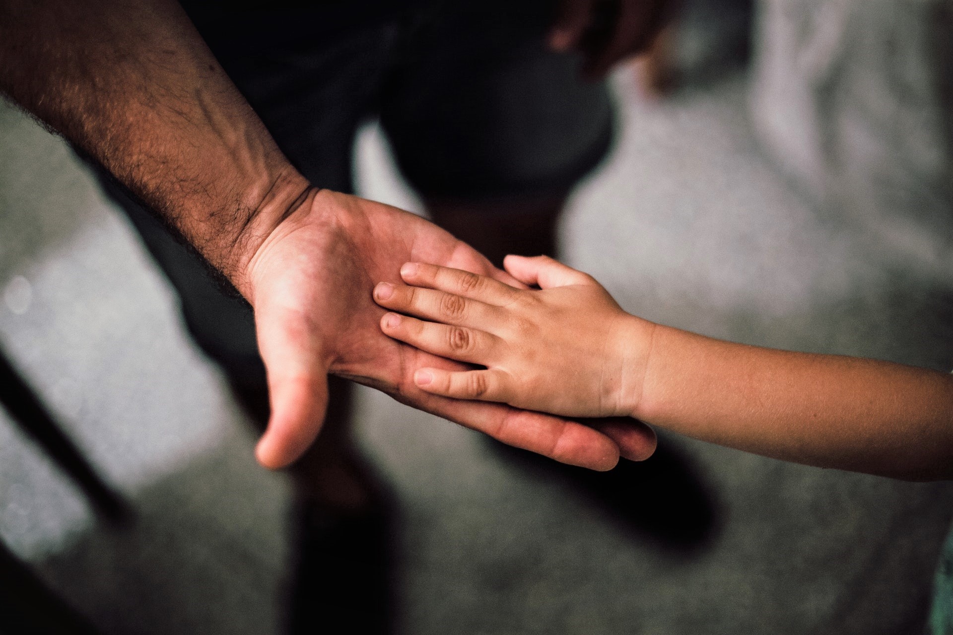 mão masculina de adulto apoia mão de criança numa imagem em close