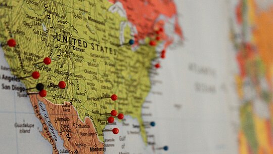 A imagem mostra um mapa, com os Estados Unidos em evidência e alguns alfinetes grudados em determinados locais. 