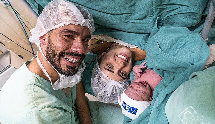 Daniel Dias, sua esposa e sua filha recém-nascida com roupas hospitalares verdes