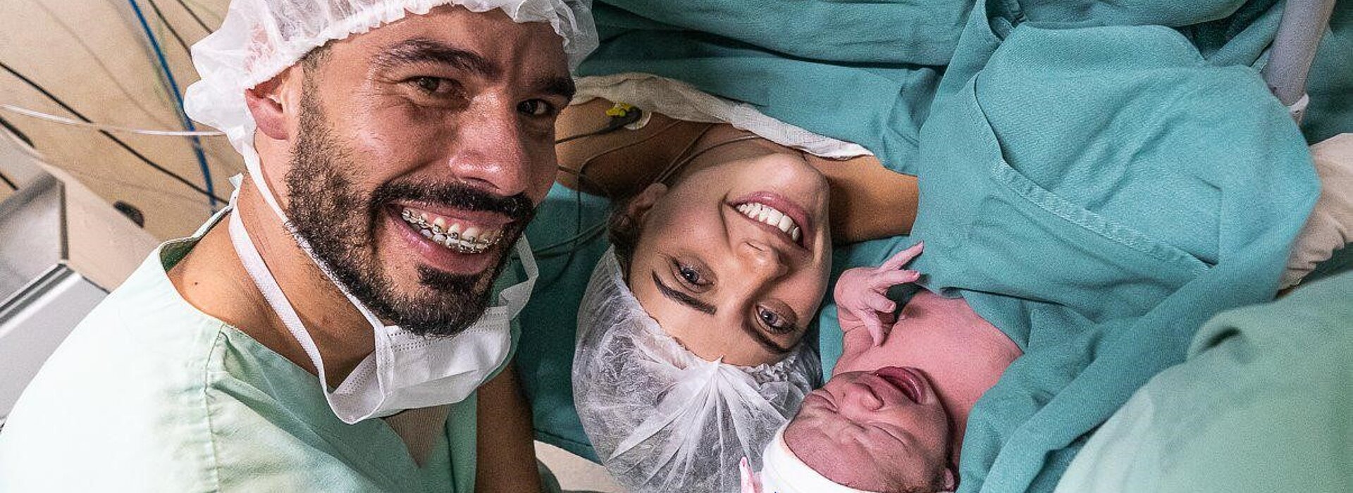Daniel Dias, sua esposa e sua filha recém-nascida com roupas hospitalares verdes