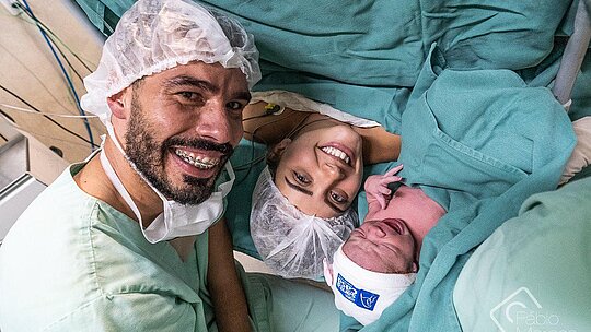Daniel Dias, sua esposa e sua filha recém-nascida com roupas hospitalares verdes