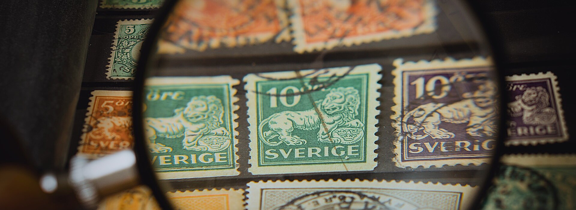 Na foto aparece uma lupa em cima de selos postais