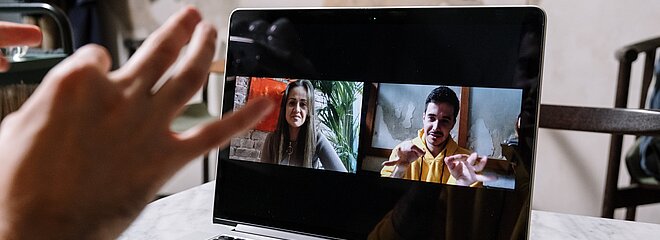 A imagem mostra um homem em uma videochamada com uma menina, eles estão converrsando em libras e a foto foca no notebook, mostrando a conversa. 