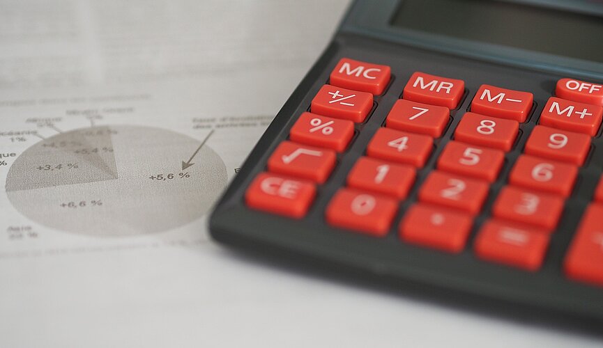 papel com gráficos sobre uma mesa ao lado de uma calculadora de teclas vermelhas.