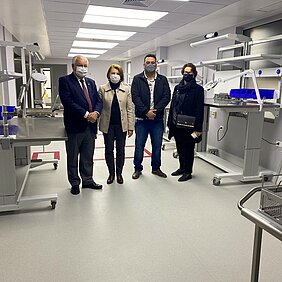 dois homens e duas mulheres de máscara estão de pé em uma sala de esterilização de materiais onde se pode ver objetos hospitalares novos