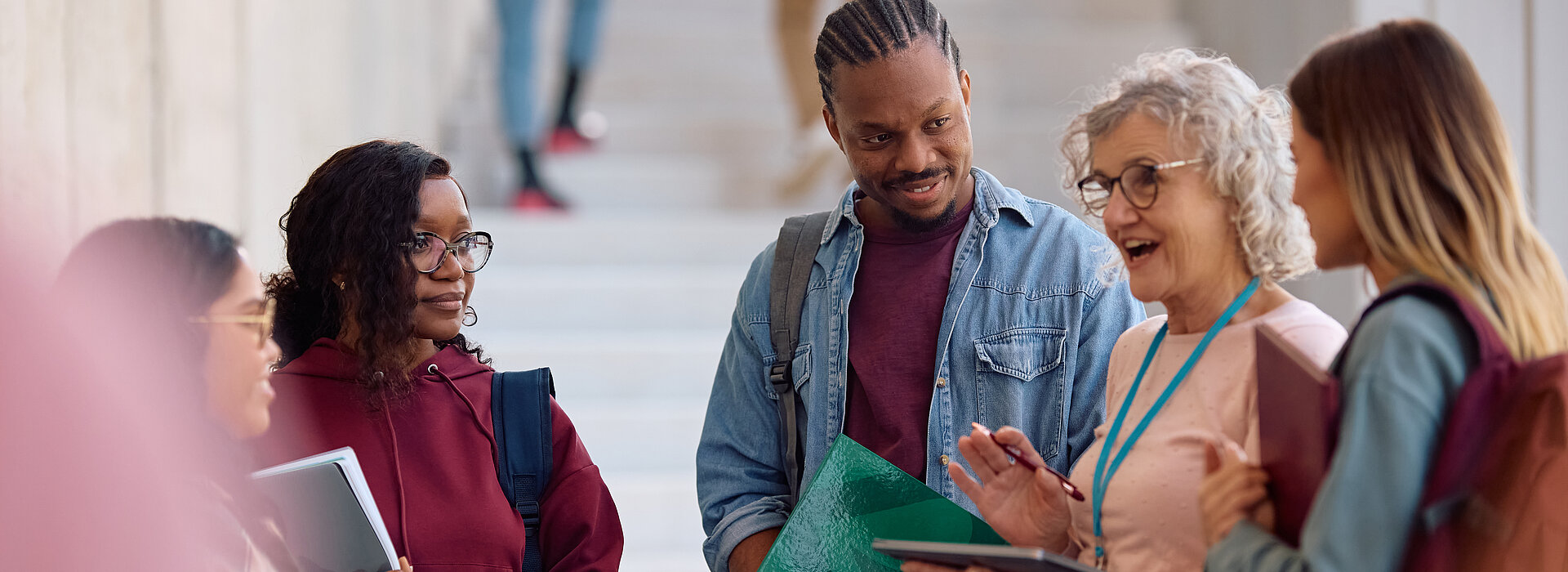 A imagem contem um grupo de jovens estudantes escutando sua professora em um local aberto.