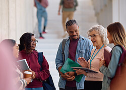 A imagem contem um grupo de jovens estudantes escutando sua professora em um local aberto.