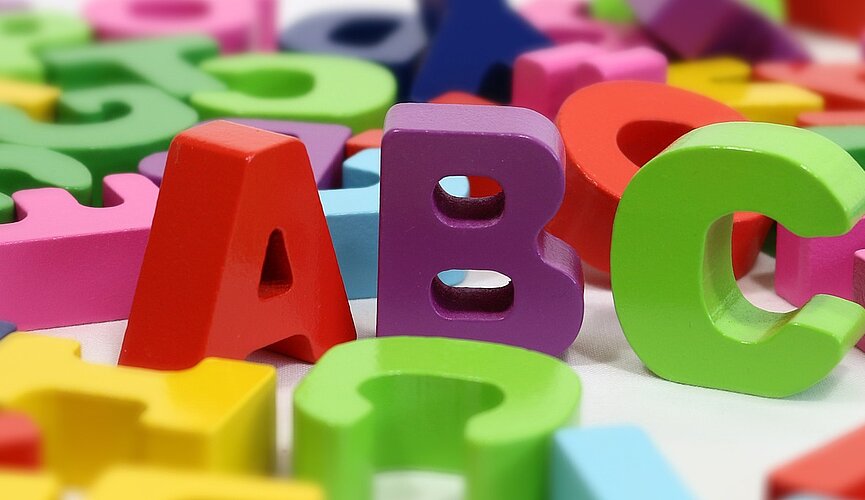letras coloridas embaralhadas ao fundo, com destaque para as letras A, B e C em primeiro plano