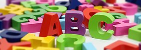 letras coloridas embaralhadas ao fundo, com destaque para as letras A, B e C em primeiro plano