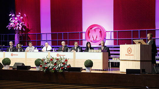 Autoridades sentadas à mesa enquanto a paraninfa discursa ao púlpito