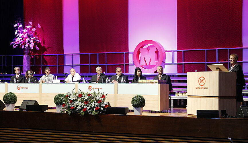 Autoridades sentadas à mesa enquanto a paraninfa discursa ao púlpito