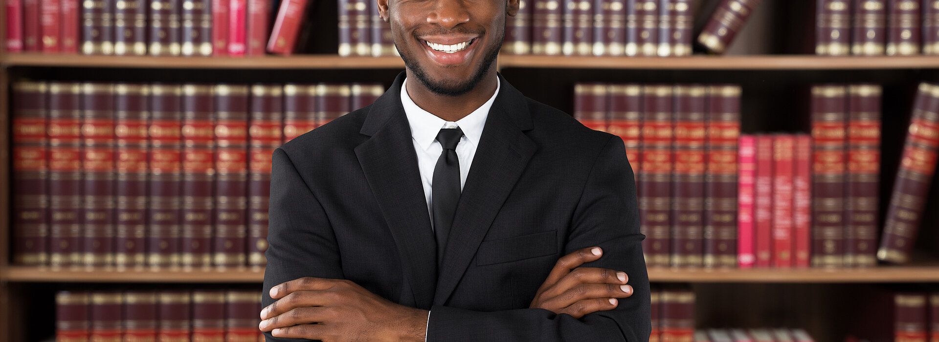 homem sorrindo de braços cruzados em frente uma estante de livros