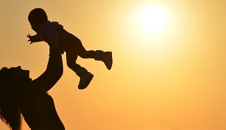 mulher segura seu filho no alto na praia com por do sol ao fundo
