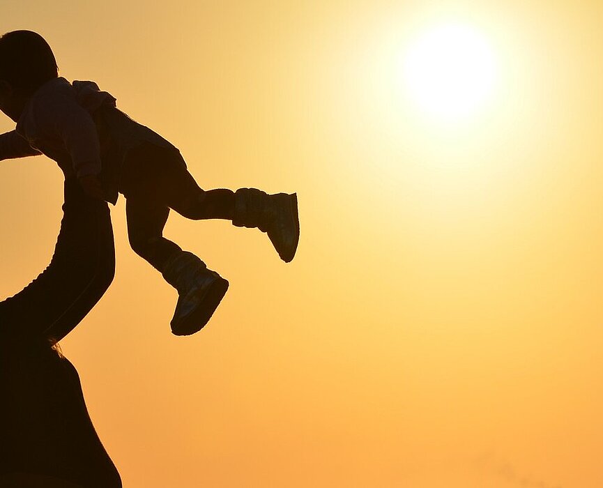 mulher segura seu filho no alto na praia com por do sol ao fundo
