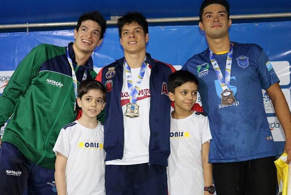 Três homens sorrindo para a foto com medalhas nas mãos