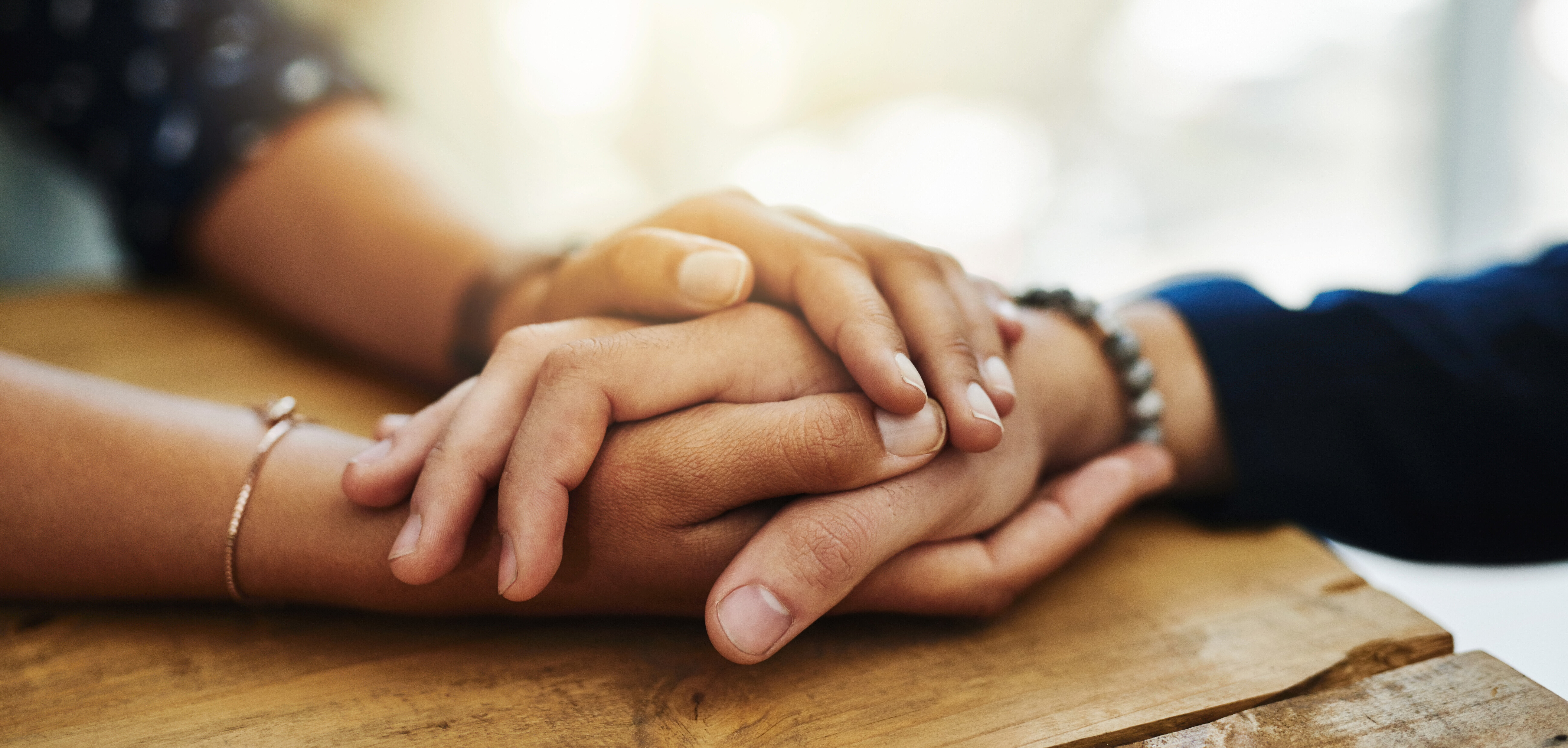 Duas pessoas segurando as mãos, apoiadas em uma mesa.