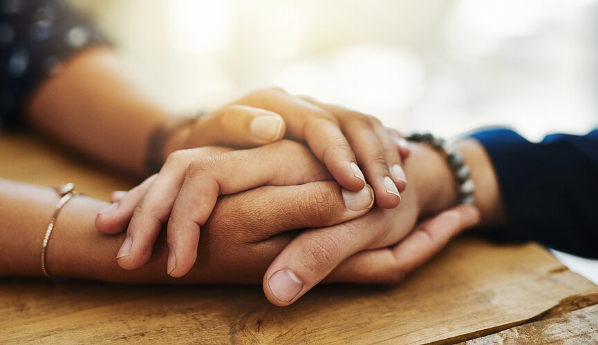 Duas pessoas segurando as mãos, apoiadas em uma mesa.