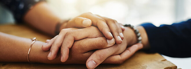 Duas pessoas segurando as mãos, apoiadas em uma mesa.