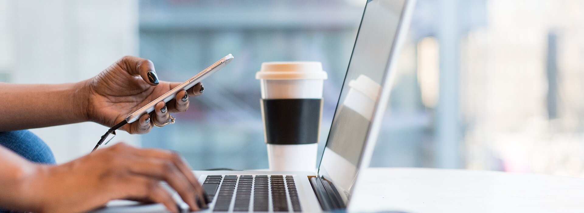 Mão de uma mulher no notebook com um óculos e café do lado