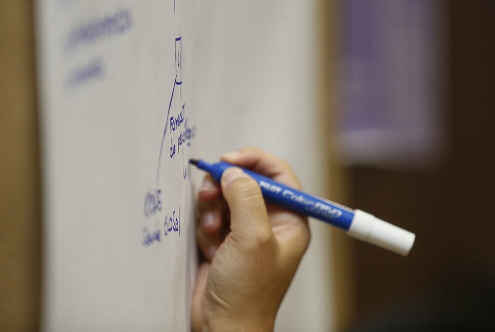 mão segurando caneta azul e escrevendo em um quadro branco