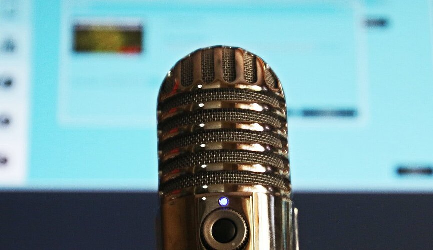 microfone em primeiro plano com uma tela de computador azulada desfocada ao fundo