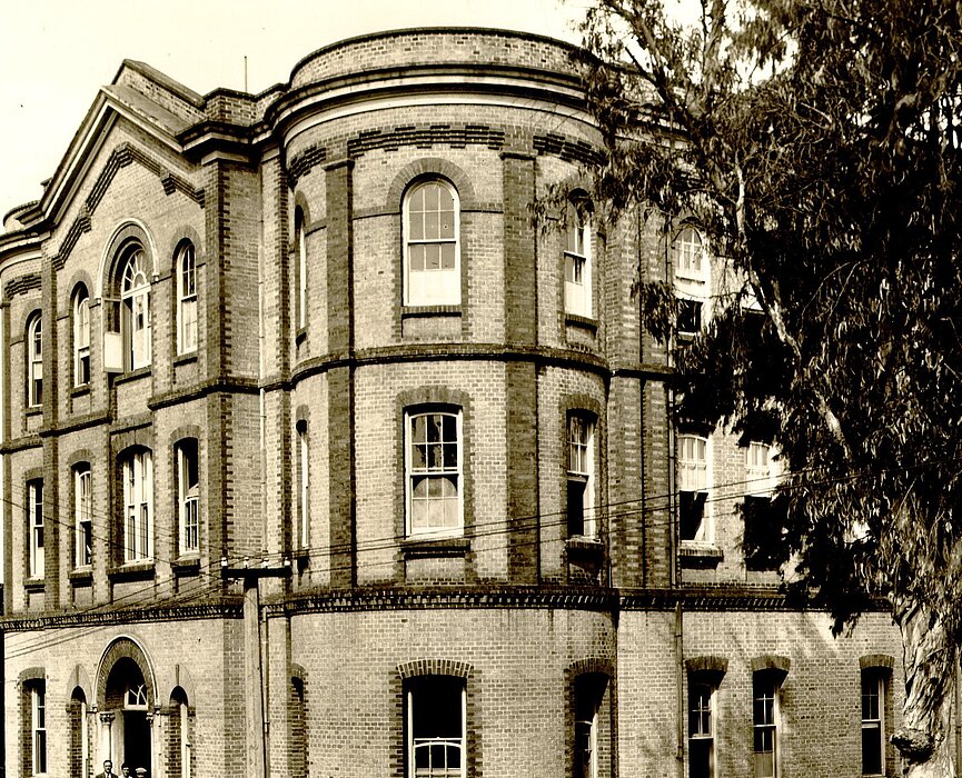 A foto é antiga e mostra o prédio Chamberlain, do campus Higienópolis. Do lado direito, na frente do prédio, tem uma árvore. Já do lado esquerdo, uma árvore está ao fundo da imagem. 