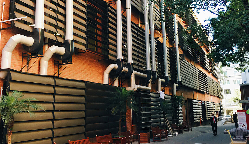 A foto mostra um prédio do campus Higienópolis, com tijolos e detalhes em preto. Uma árvore está do lado direito da foto.