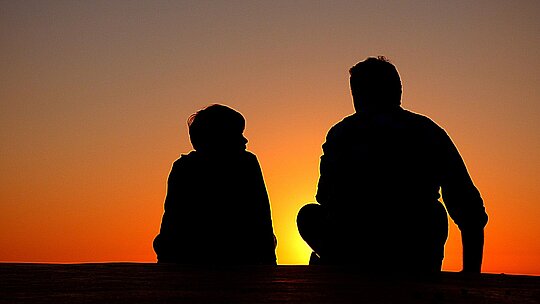 silhueta de pai e filho sentados contra um por do sol