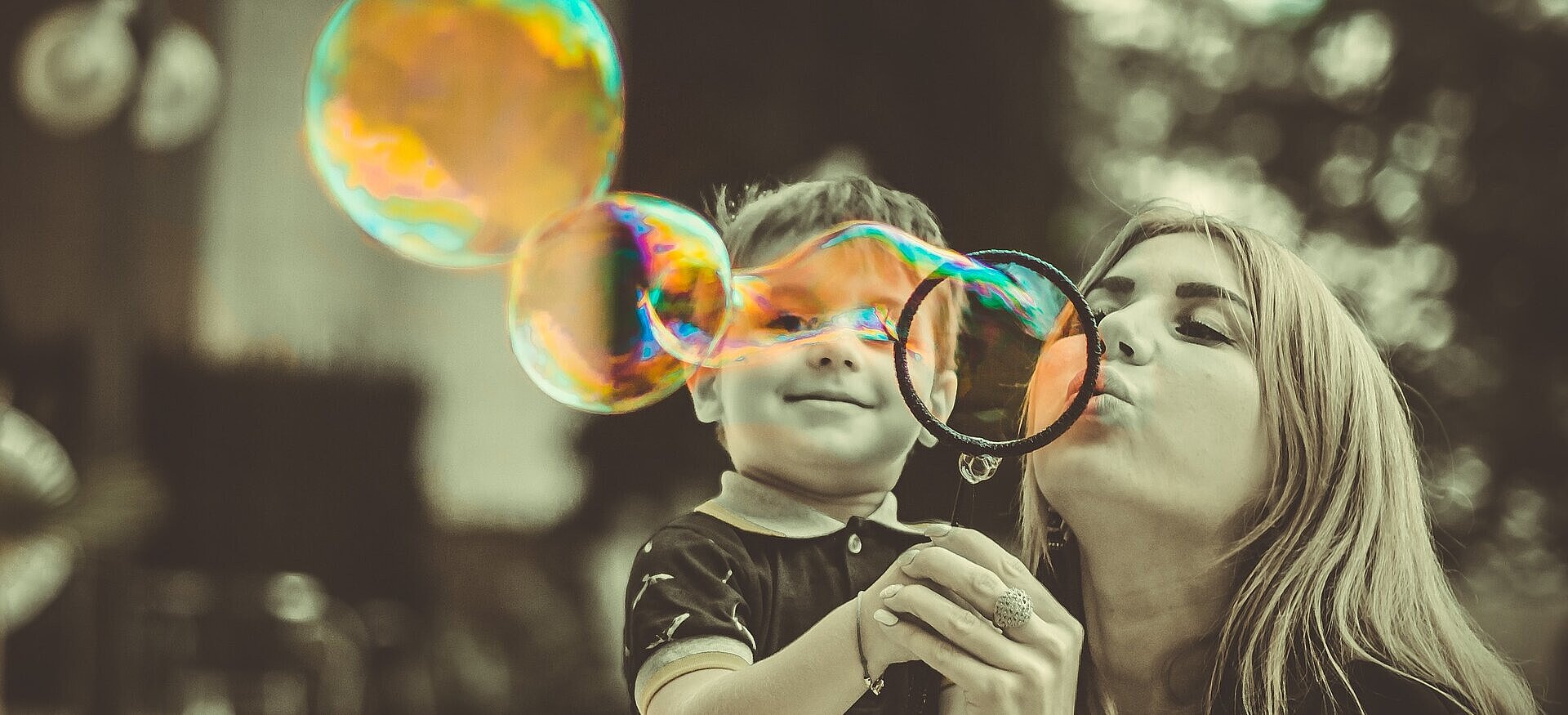 Mulher fazendo bola de sabão ao lado de um menino.