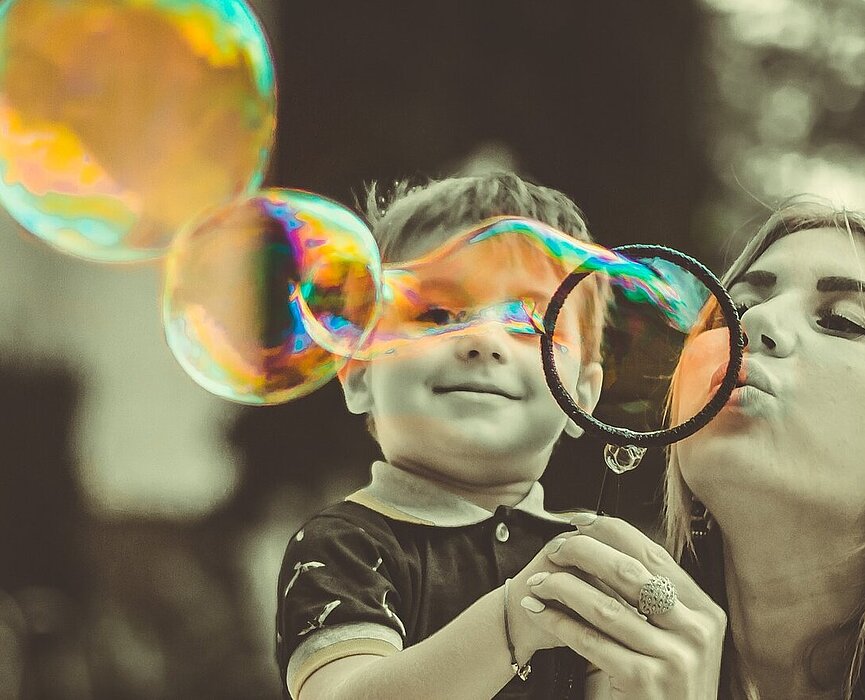 Mulher fazendo bola de sabão ao lado de um menino.