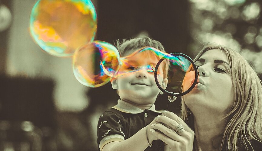 Mulher fazendo bola de sabão ao lado de um menino.