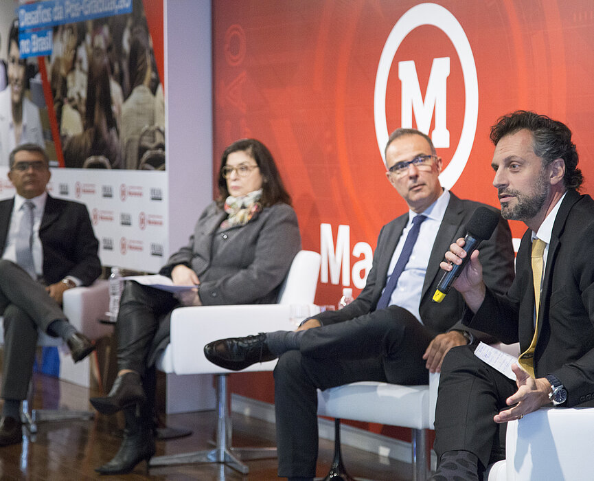 especialistas debatem no palco. Plateia cheia