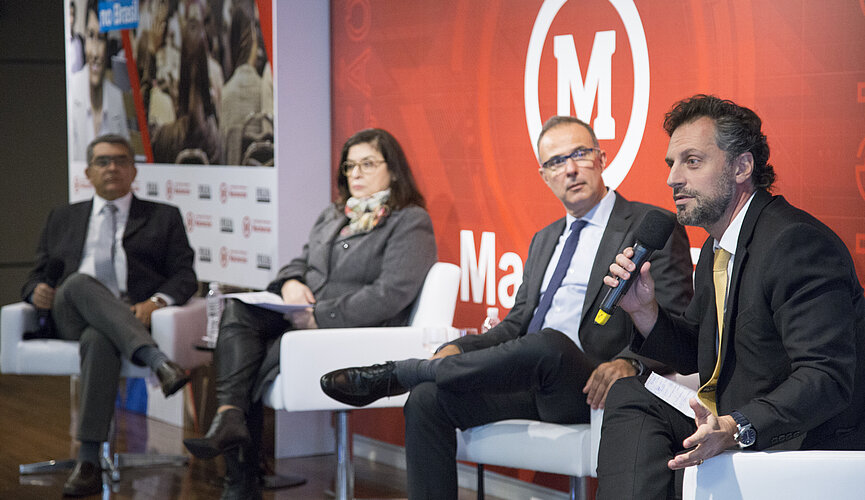 especialistas debatem no palco. Plateia cheia
