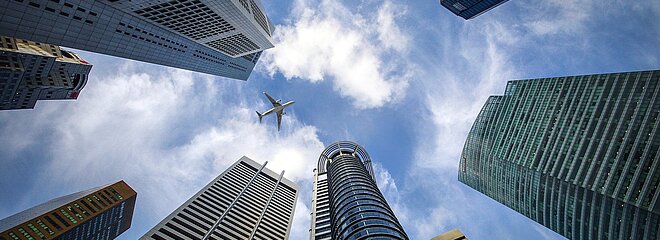 Imagem feita de baixo para cima mostrando vários prédios e um avião passando no céu