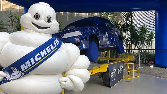 Mascote da Michelin ao lado do estande com simulador
