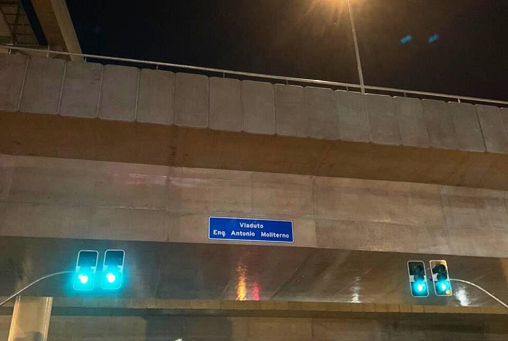 Imagem de uma avenida com carros passando e um viaduto passando sobre ela no qual se pode ler, em uma placa azul com dizeres em branco, "engenheiro Antonio Moliterno"