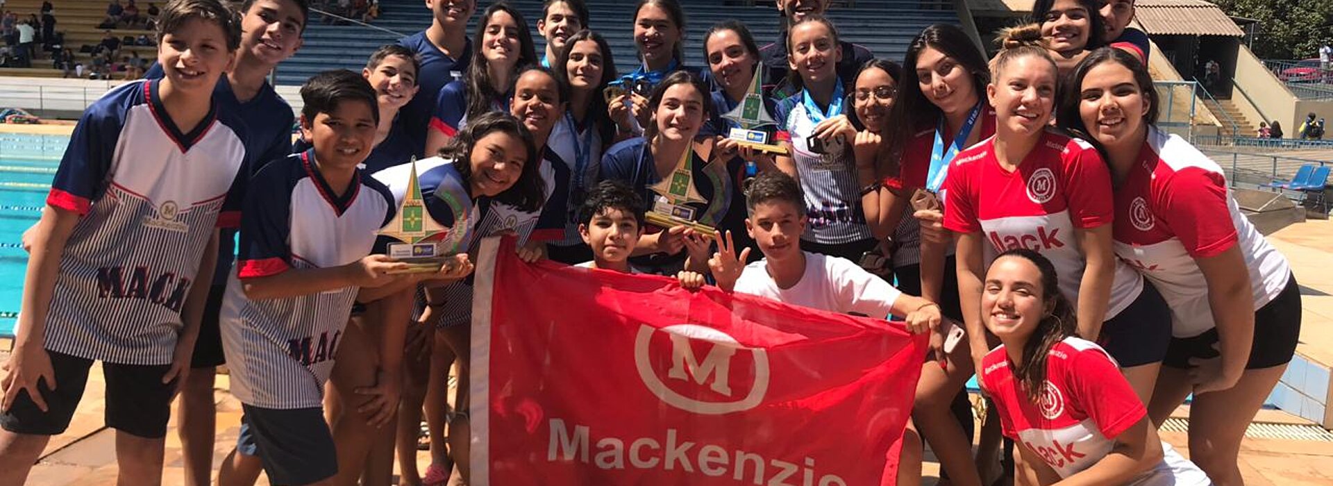 Jovens atletas em pé com bandeira do Mackenzie ao centro