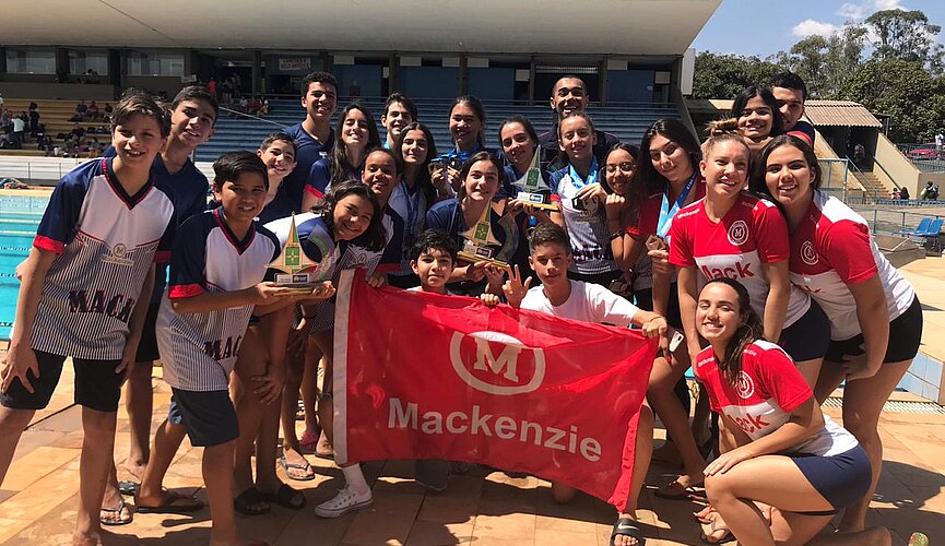 Jovens atletas em pé com bandeira do Mackenzie ao centro