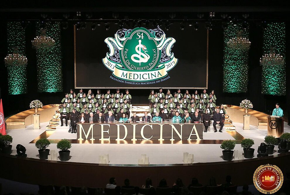 formandos sentados no palco com telão ao fundo