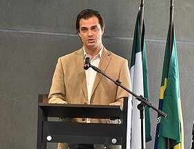 Pedro Buck está falando no pulpito em cima do palco. Atrás dele está a bandeira do Brasil.