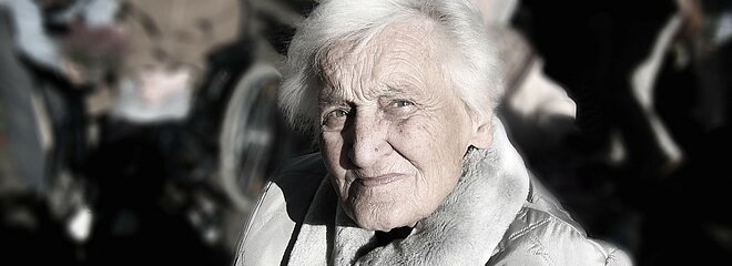 Na foto, mostra uma senhora olhando para a câmera