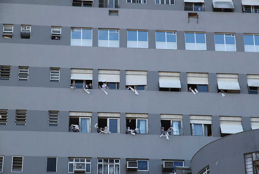várias mãos com lenços brancos saindo das janelas do hospital em aceno