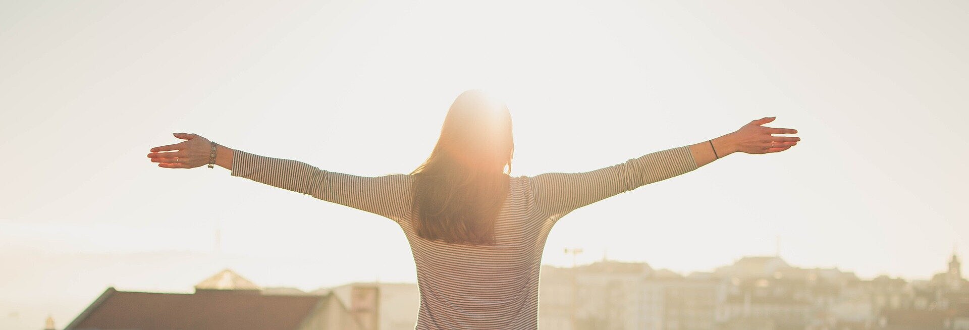Mulher com os braços abertos olhando o horizonte.