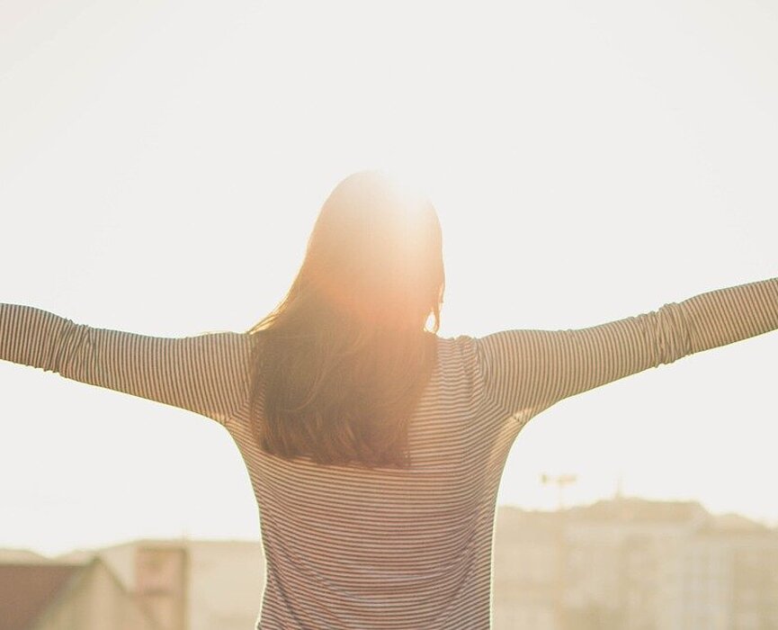 Mulher com os braços abertos olhando o horizonte.