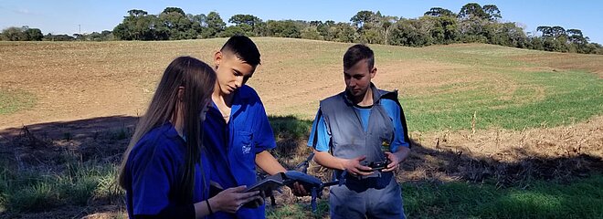 Três pessoas em uma fazenda com um drone na mão 