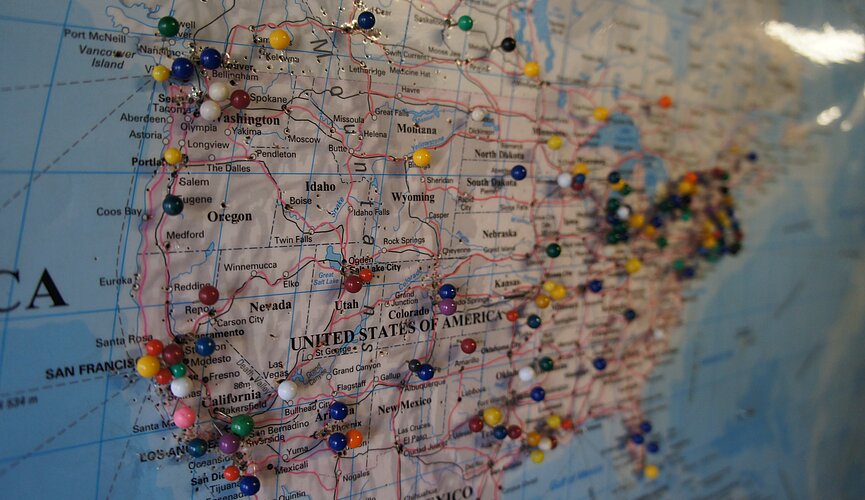 Foto mostra o mapa dos Estados Unidos com vários alfinetes redondos coloridos.  