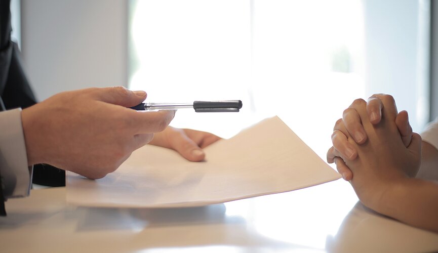 A imagem apresenta uma pessoa prestes a assinar um contrato de emprego. 