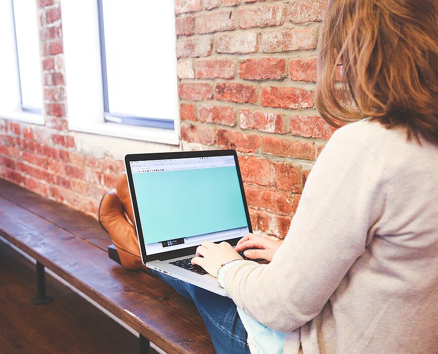 Uma menina mexe no notebook sentada próxima de uma janela