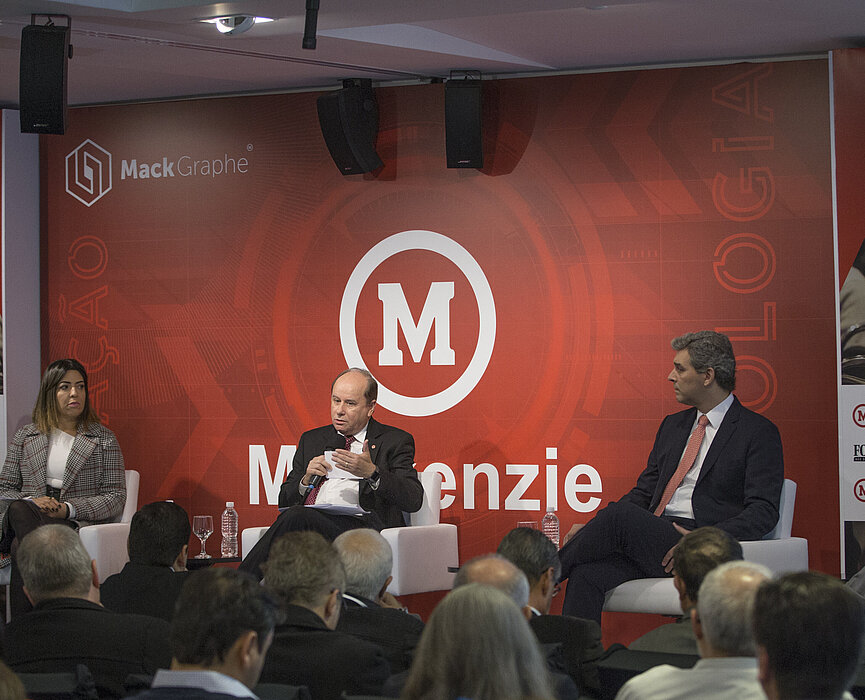 autoridades debatendo no palco com plateia cheia